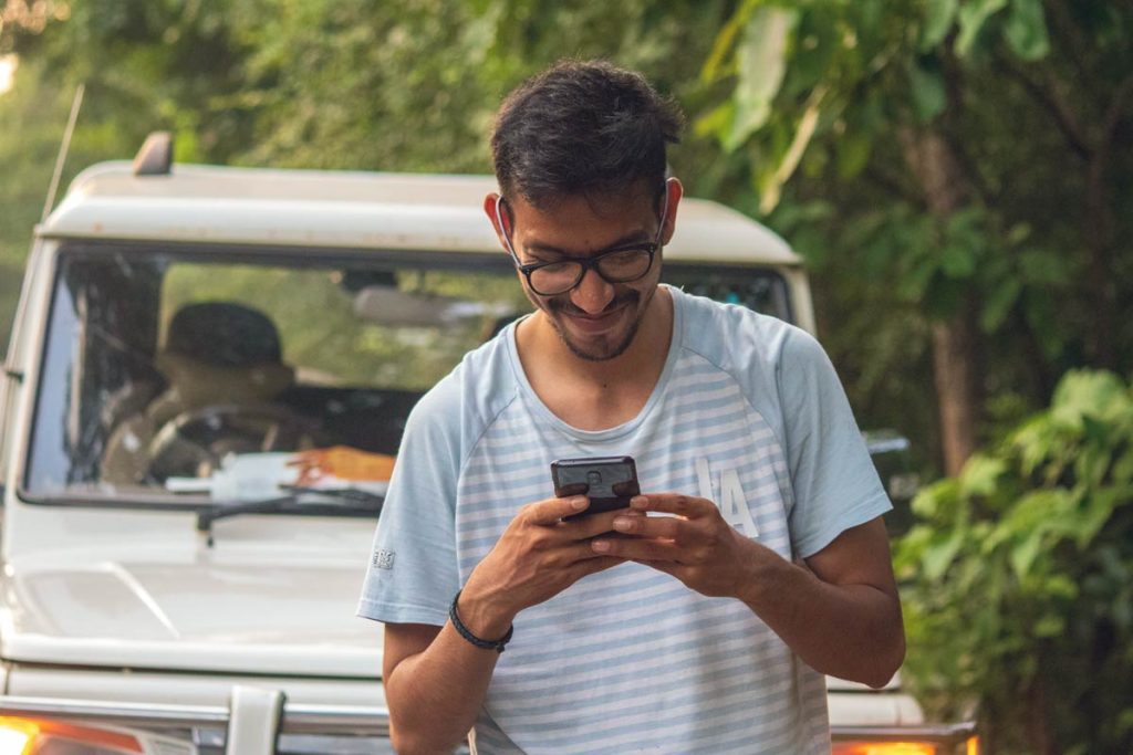 A man connecting to others in front of a car on penpal on his phone