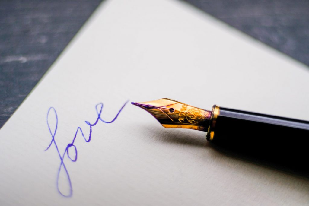 An ink pen lies beside a letter with the single blue word, love written on it
