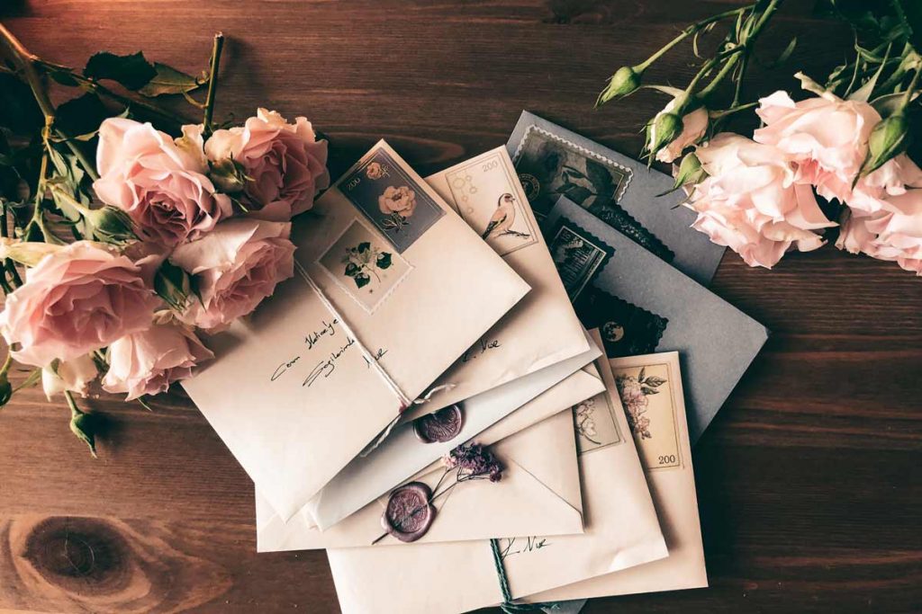 A pile of letters unopened on a table with flowers next to the them.